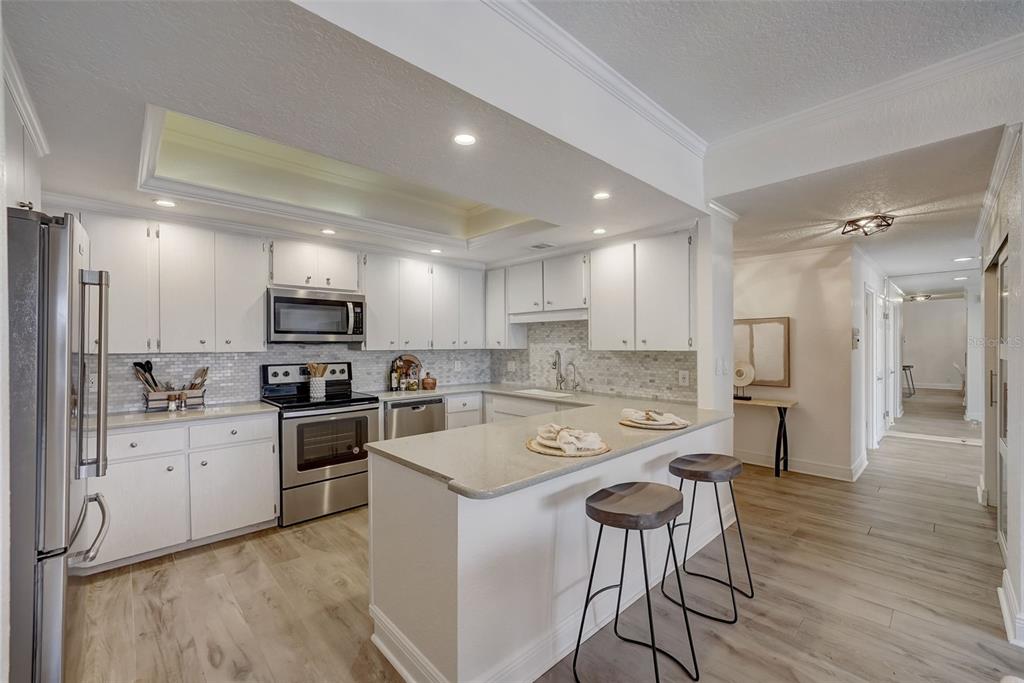 A kitchen features white cabinets, stainless steel appliances, a breakfast bar, and light wood flooring — 6 BELLEVIEW BOULEVARD UNIT 101, BELLEAIR, FL
