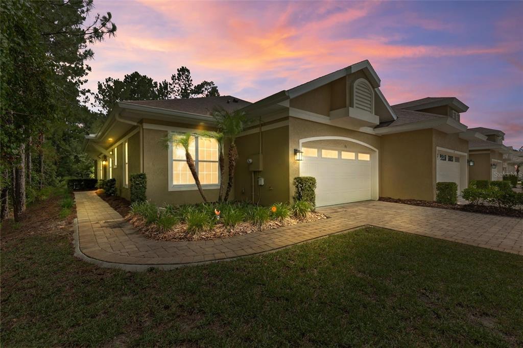 A tan single-story house with a two-car garage and a paved walkway at dusk — 46 HERON WING DRIVE, ORMOND BEACH, FL