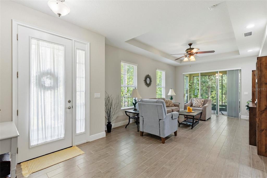 A bright living room features light tile flooring, a tray ceiling, and a glass sliding door — 46 HERON WING DRIVE, ORMOND BEACH, FL