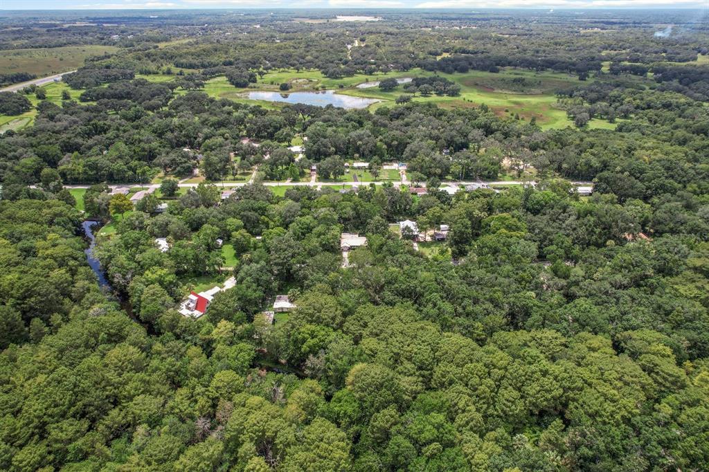 An aerial view shows a house with a red roof surrounded by dense forest — 523 S TUCK POINT, INVERNESS, FL