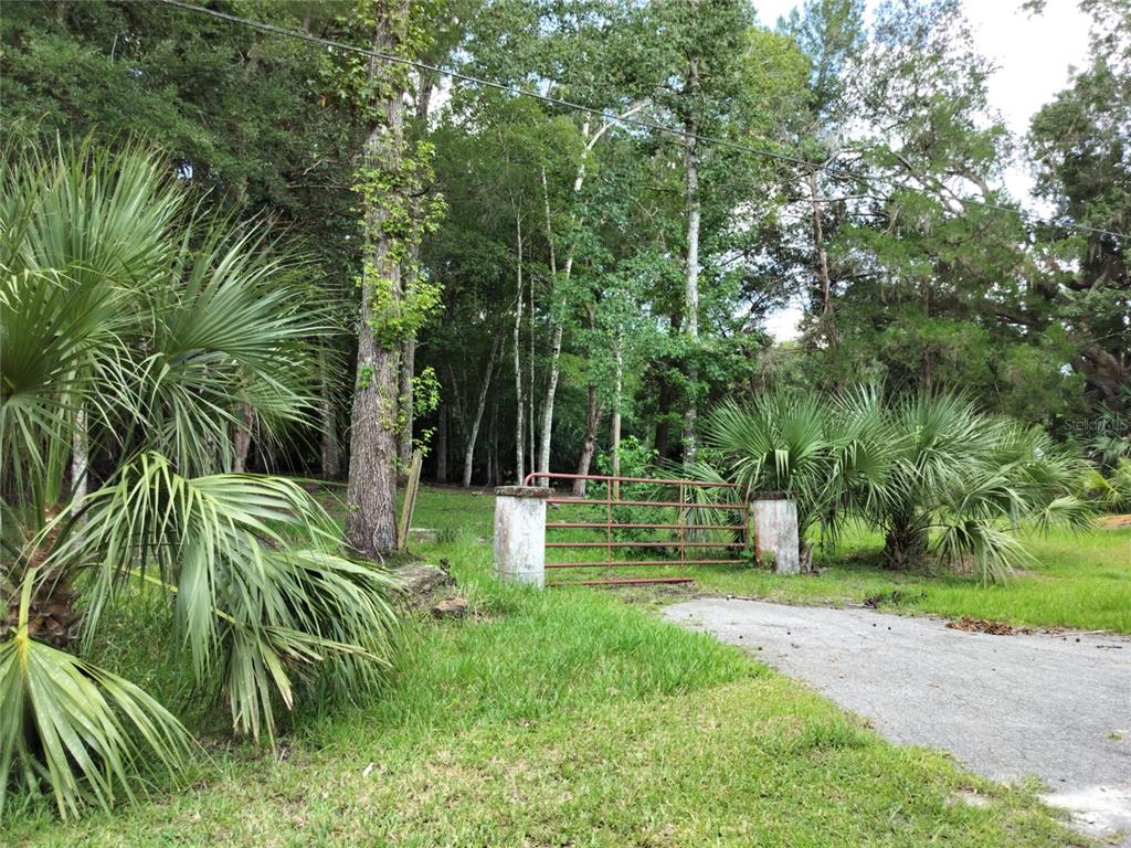A red metal gate stands between two concrete pillars at the entrance to a wooded lot — 523 S TUCK POINT, INVERNESS, FL