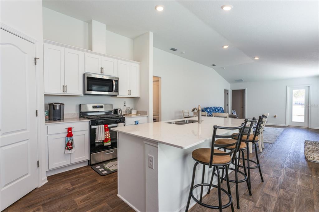 A kitchen features white cabinets, stainless steel appliances, a quartz island, and wood-look flooring — 18 BOGEY PLACE, BUNNELL, FL