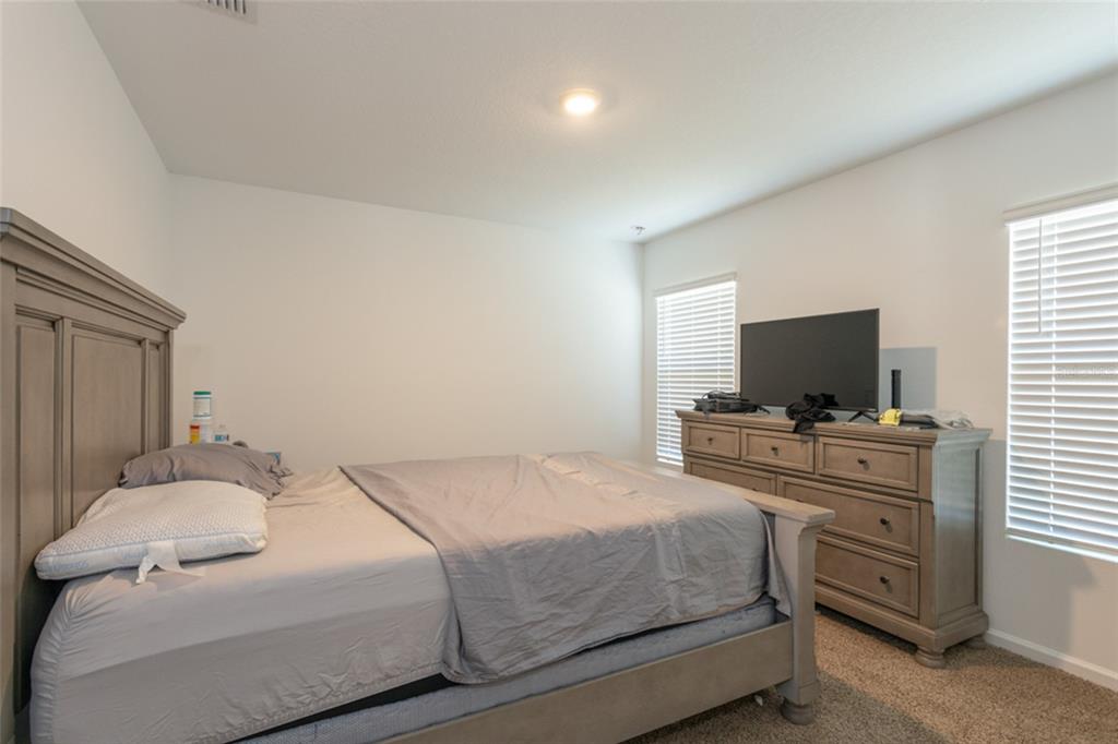 A bedroom features a wooden bed frame, a matching dresser with a television, and carpeted flooring — 18 BOGEY PLACE, BUNNELL, FL