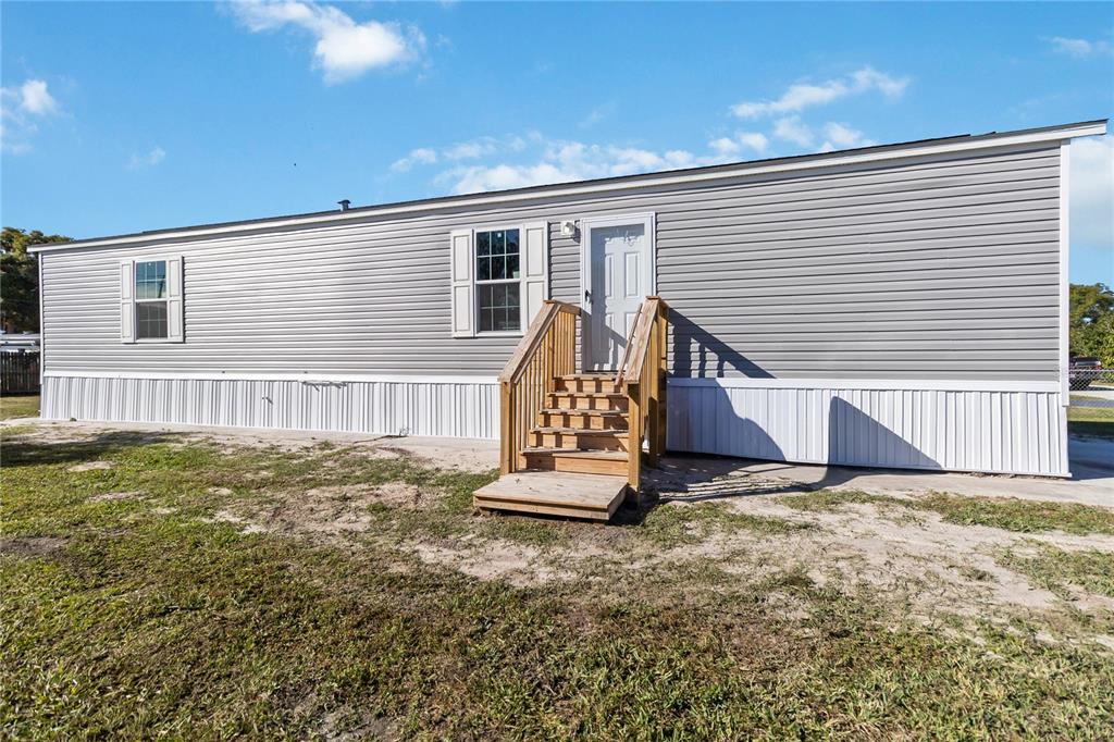 A gray mobile home exterior features white skirting, a wooden staircase, and two windows — 2003 OAK STREET, ST CLOUD, FL