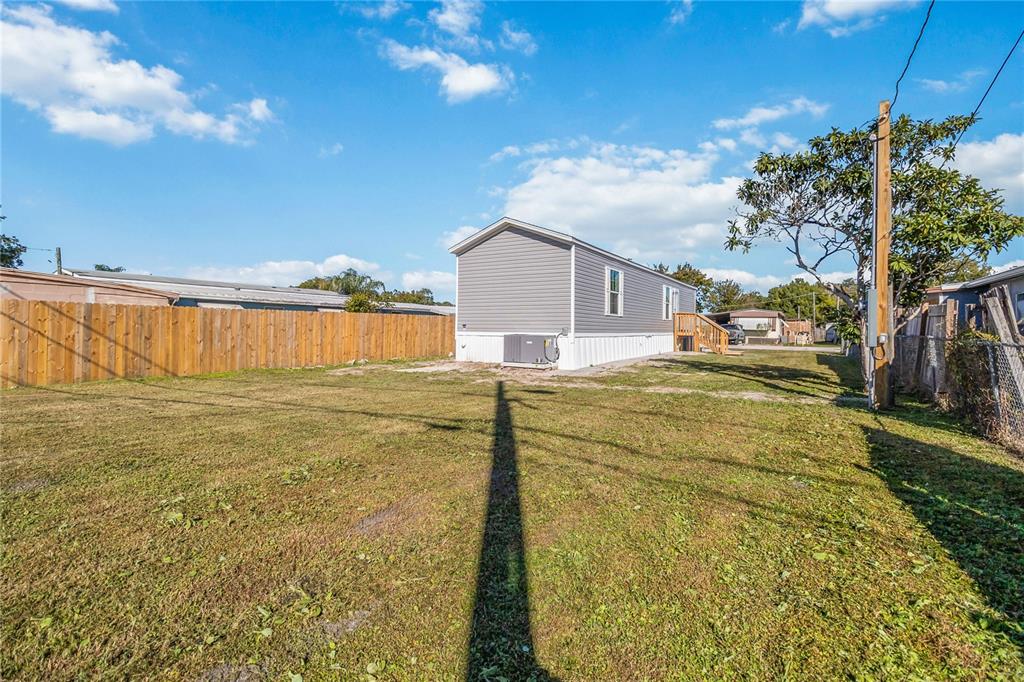 A gray mobile home sits on a grassy lot enclosed by wooden and chain-link fences — 2003 OAK STREET, ST CLOUD, FL