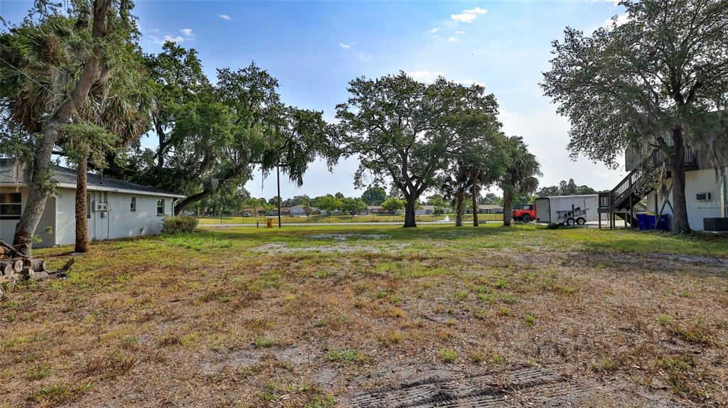 A grassy, partially cleared lot sits between two buildings with mature trees in the background — 1802 N FERN PALM DRIVE, EDGEWATER, FL
