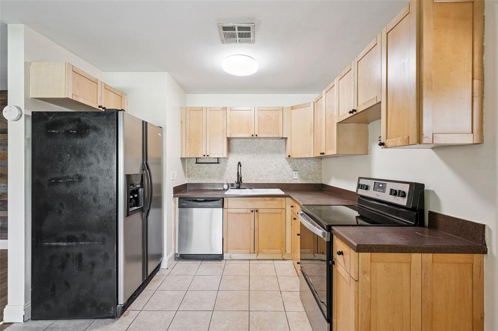 A kitchen features light wood cabinets, dark countertops, stainless steel appliances, and tiled flooring — 509 HILLSIDE AVENUE, ORLANDO, FL
