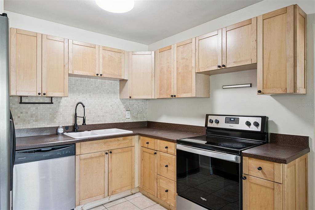 A kitchen featuring light wood cabinets, dark countertops, stainless steel appliances, and a tiled backsplash — 509 HILLSIDE AVENUE, ORLANDO, FL
