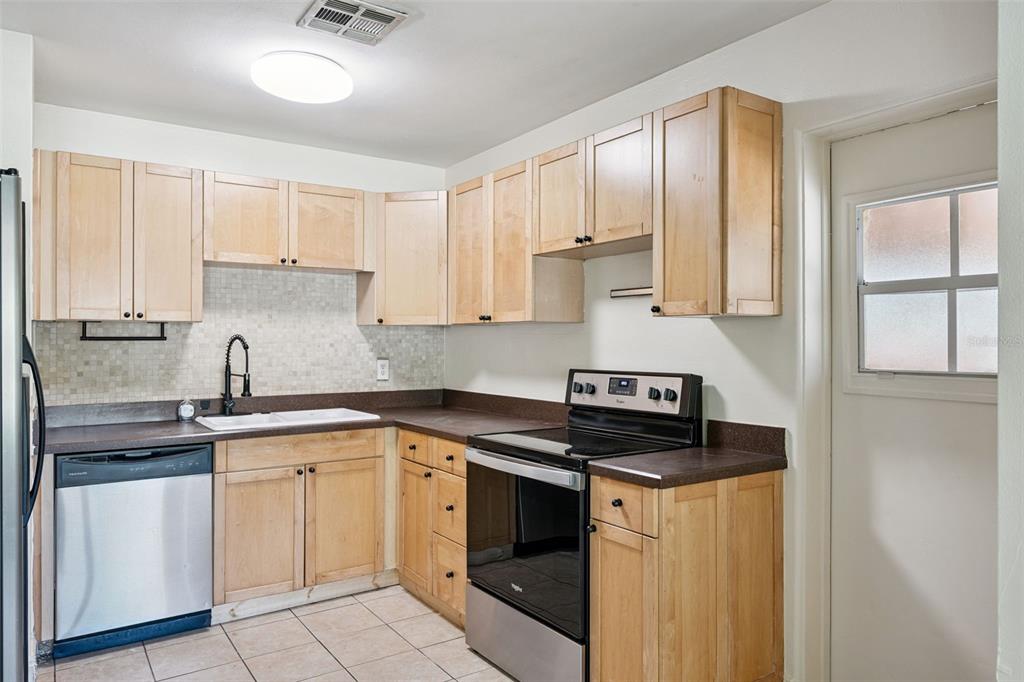 A kitchen with light wood cabinets, stainless steel appliances, dark countertops, and a tiled backsplash — 509 HILLSIDE AVENUE, ORLANDO, FL