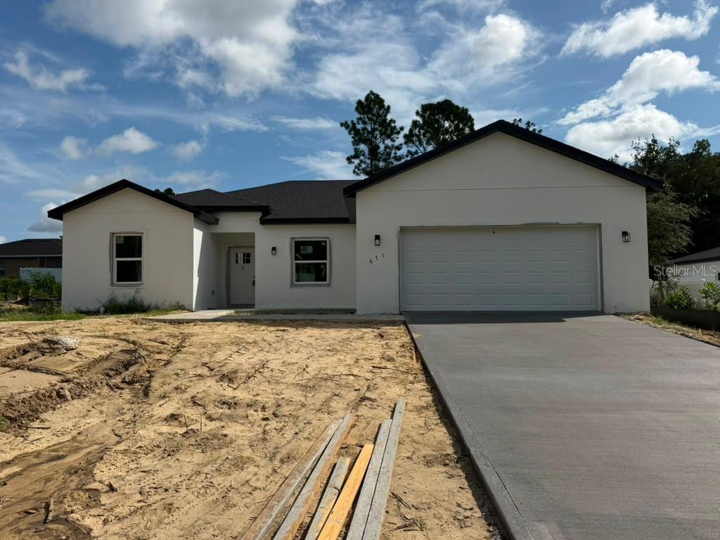 A newly constructed single-story house with a white stucco exterior, dark roof, and concrete driveway — 671 MARION OAKS MANOR, OCALA, FL