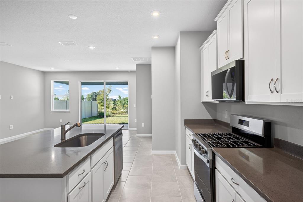 A modern kitchen features white cabinets, dark countertops, a center island, and stainless steel appliances — 13129 OXEYE LANE, PARRISH, FL