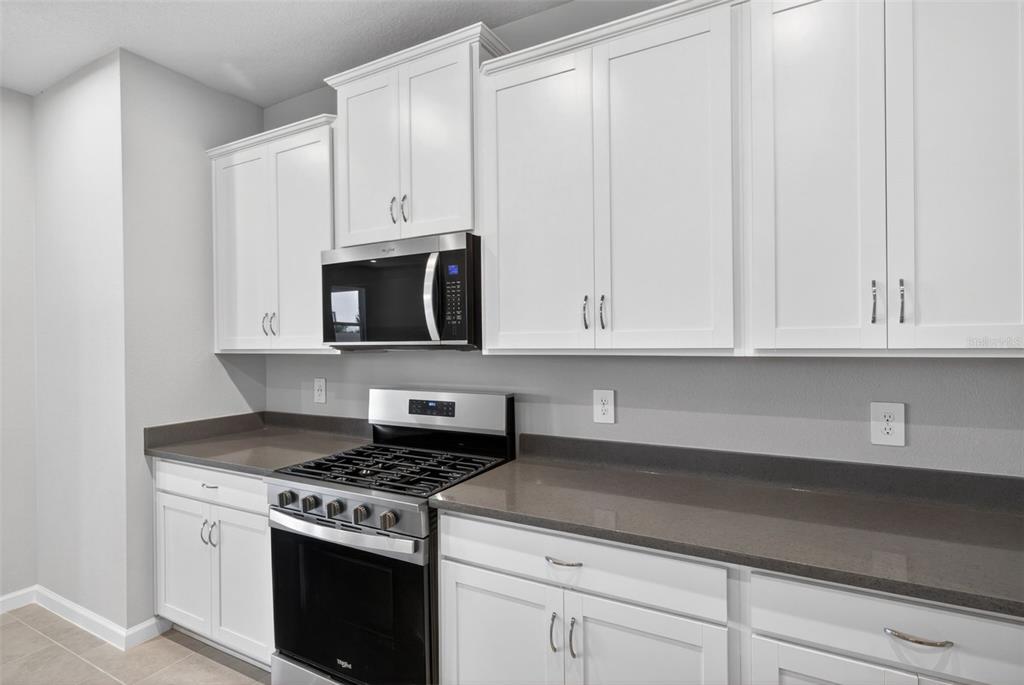 A kitchen features white shaker cabinets, a stainless steel stove, and dark gray countertops — 13129 OXEYE LANE, PARRISH, FL