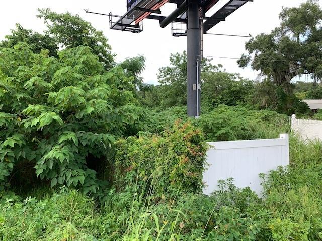 A large billboard stands behind a white vinyl fence surrounded by overgrown trees and vegetation — 2607 E SEMORAN BOULEVARD, APOPKA, FL