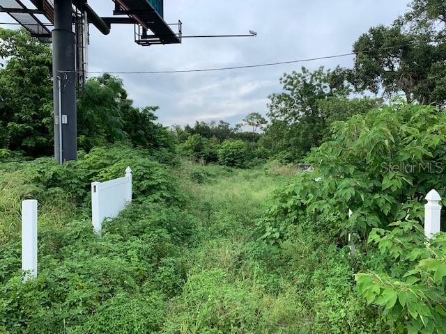 An overgrown lot features a tall billboard support structure and white vinyl fence posts — 2607 E SEMORAN BOULEVARD, APOPKA, FL