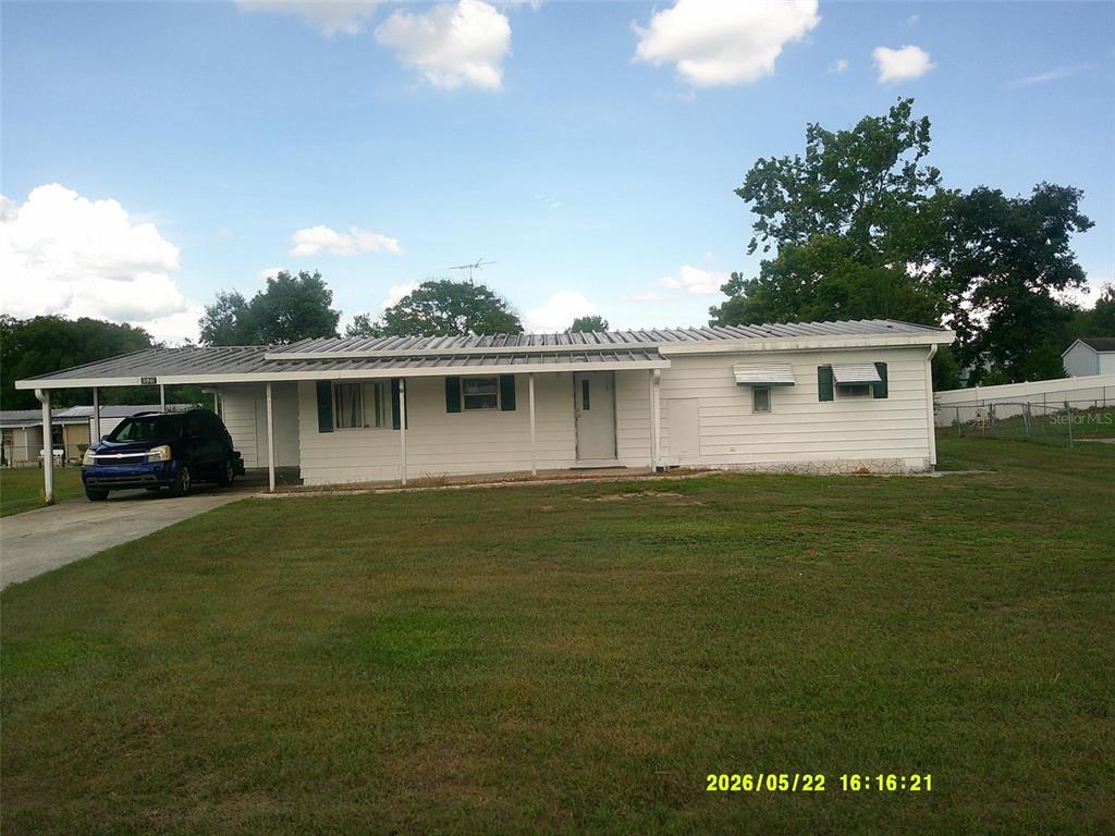 A white, single-story house with a metal roof and an attached carport sits on grass — 15211 SE 104TH COURT, SUMMERFIELD, FL