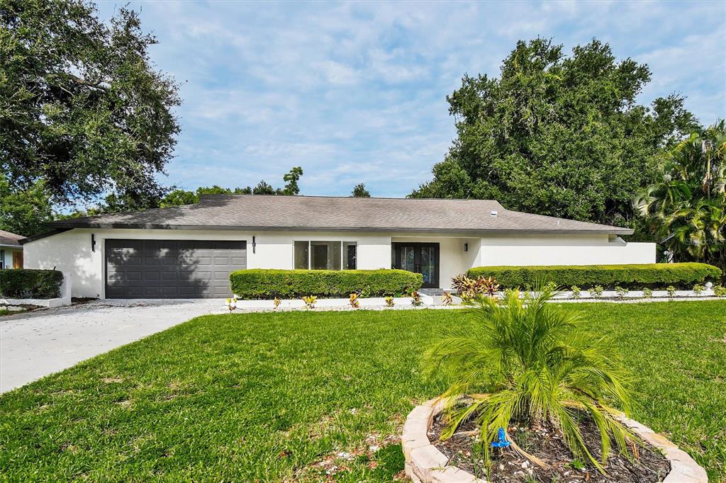 A single-story house with a gray garage door and a concrete driveway sits on grass — 207 DUNBRIDGE DRIVE, PALM HARBOR, FL