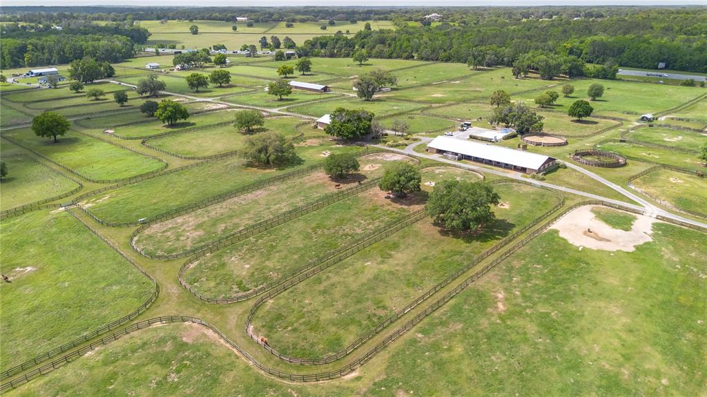 An aerial view of a horse farm featuring fenced pastures, a long barn, and trees — 5100 W HWY 329, REDDICK, FL