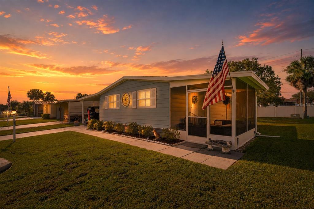 A light blue mobile home with a screened-in porch and an American flag at sunset — 606 TARRSON BOULEVARD, LADY LAKE, FL