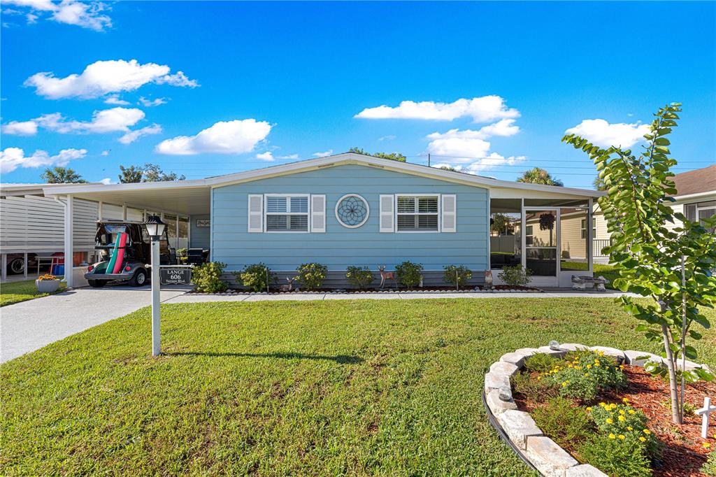 A light blue manufactured home features a carport, a front lawn, and a screened porch — 606 TARRSON BOULEVARD, LADY LAKE, FL