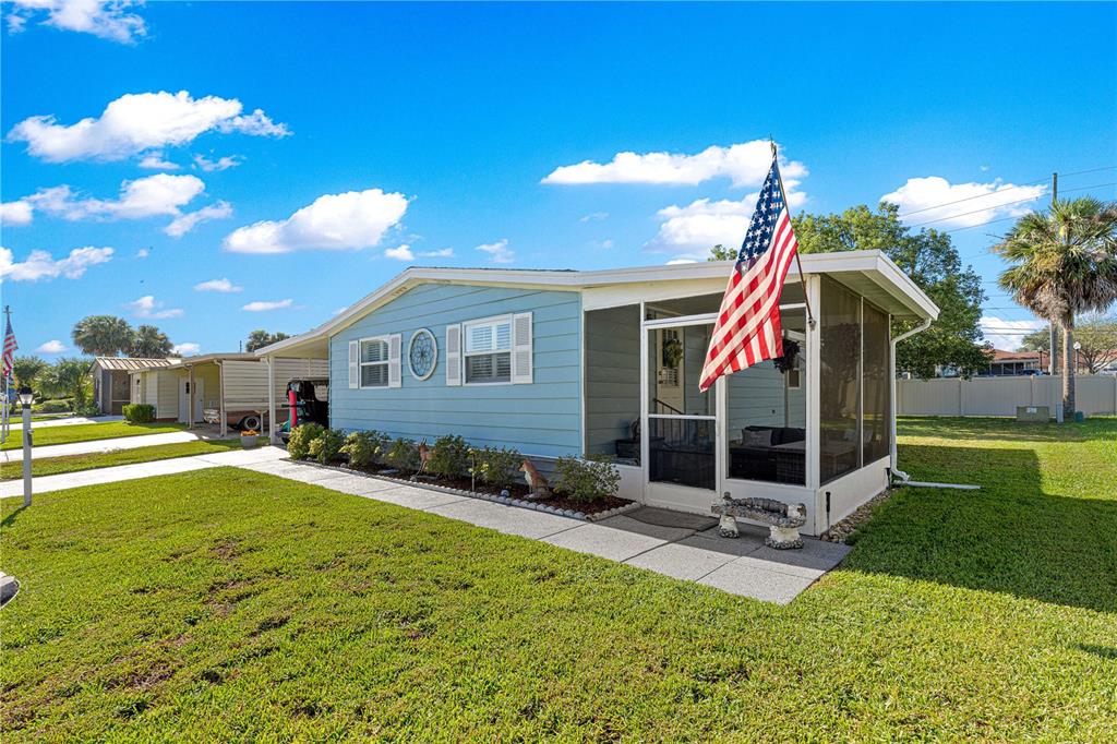 A light blue mobile home with a screened-in porch and an American flag — 606 TARRSON BOULEVARD, LADY LAKE, FL