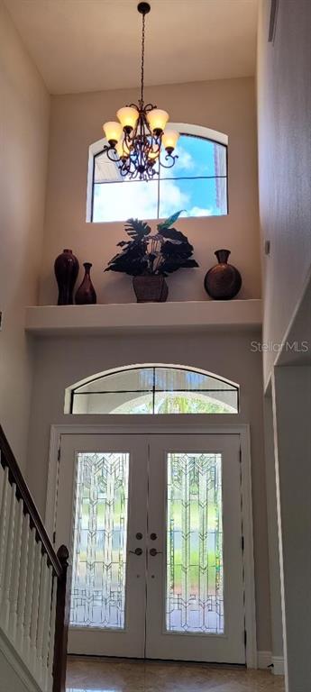 An entryway features double glass-paneled doors, a high arched window, and a decorative chandelier above — 2675 LAKEBREEZE LANE S, CLEARWATER, FL
