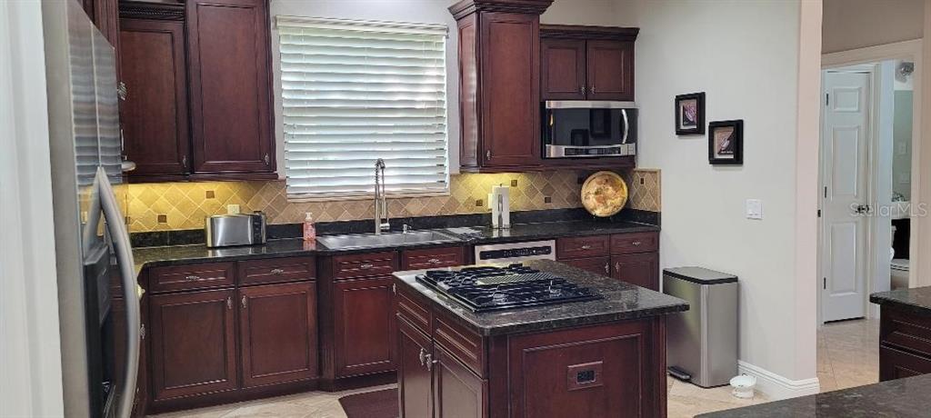 A kitchen features dark wood cabinetry, granite countertops, a center island, and stainless steel appliances — 2675 LAKEBREEZE LANE S, CLEARWATER, FL
