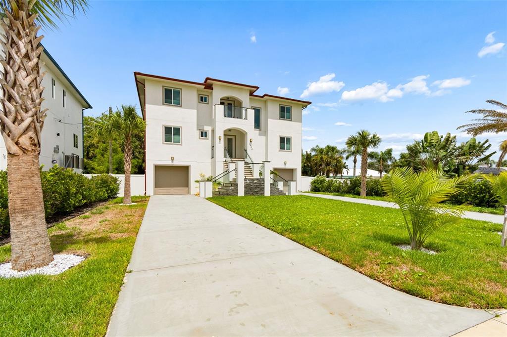 A three-story white house with a concrete driveway and palm trees in the front yard — 1964 CEDAR DRIVE, DUNEDIN, FL