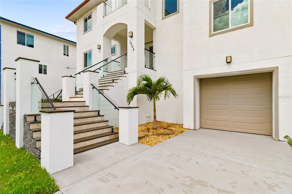 A white multi-story house exterior features a concrete driveway, a garage, and elevated stairs — 1964 CEDAR DRIVE, DUNEDIN, FL