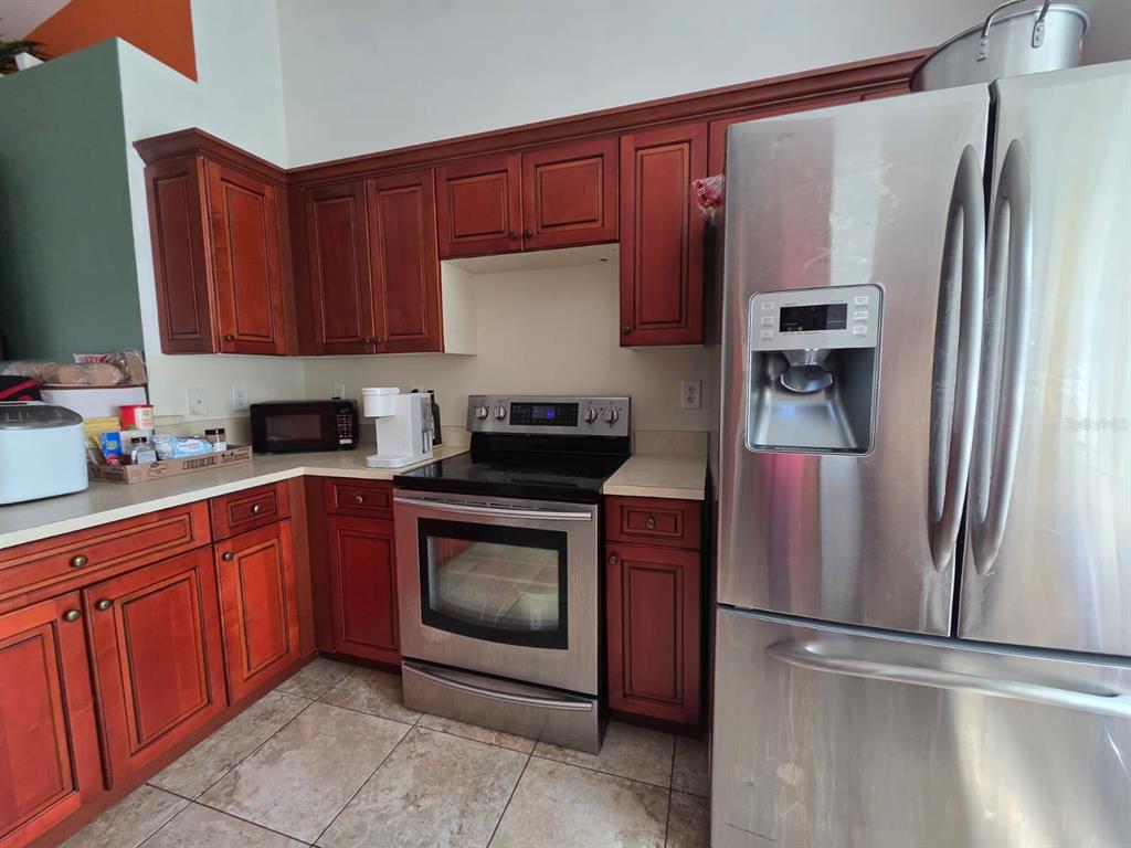 A kitchen features cherry wood cabinets, stainless steel appliances, and light-colored countertops — 3529 SUNSHINE BOULEVARD, LEHIGH ACRES, FL