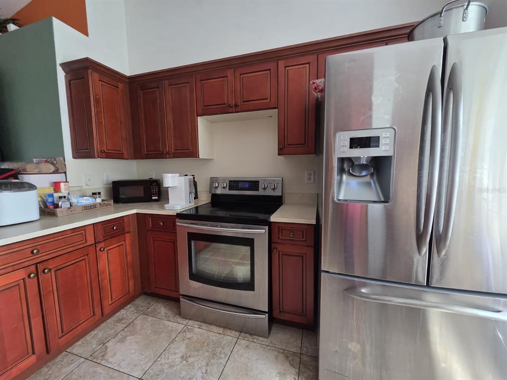 A kitchen features wood cabinets, stainless steel appliances, and tile flooring — 3529 SUNSHINE BOULEVARD, LEHIGH ACRES, FL