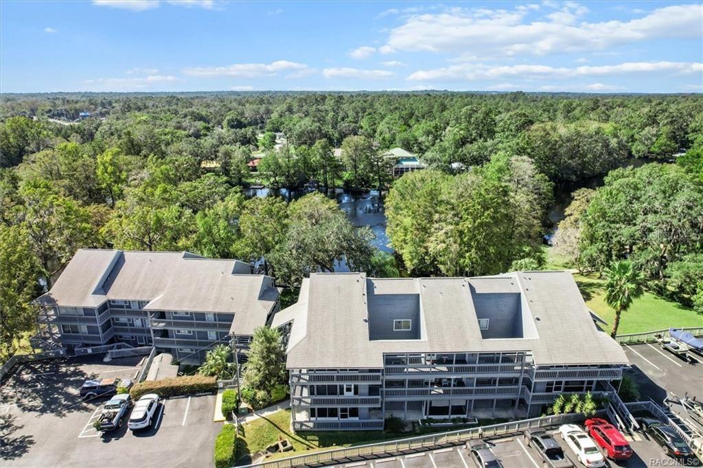 An aerial view shows two multi-story gray apartment buildings situated near a wooded riverfront — 20820 RIVER DRIVE UNIT B37, DUNNELLON, FL