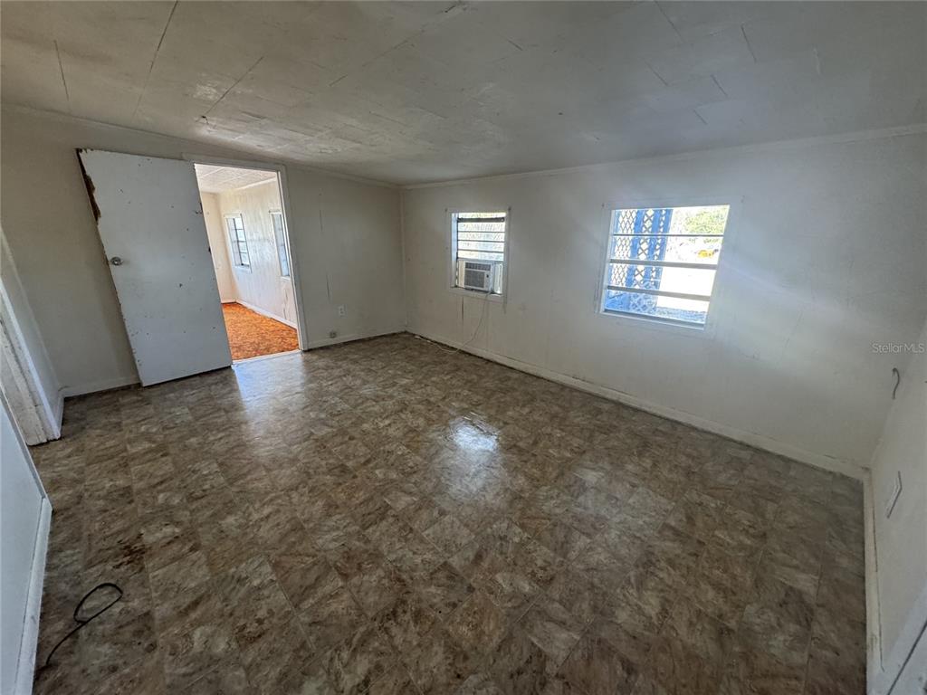 An empty room features vinyl tile flooring, white walls, and two windows with security bars — 11606 HUGGINS STREET, LEESBURG, FL
