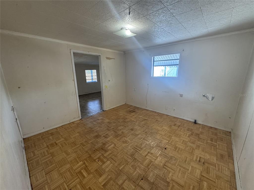 An empty room features parquet wood flooring, white walls, and a doorway to another room — 11606 HUGGINS STREET, LEESBURG, FL