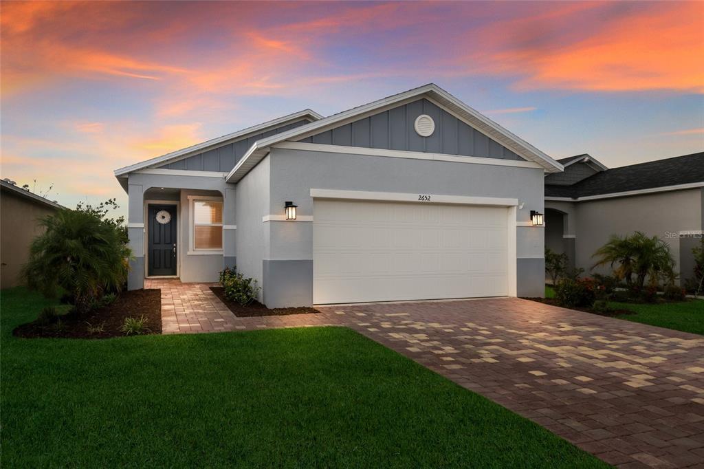 A single-story house with a two-car garage, gray siding, and a paved driveway at sunset — 2652 89TH STREET CIRCLE E, PALMETTO, FL