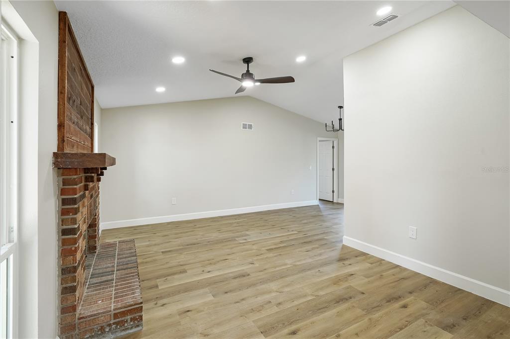 A living room with wood-look flooring, a brick fireplace, and an adjacent kitchen area — 3336 TCU BOULEVARD, ORLANDO, FL