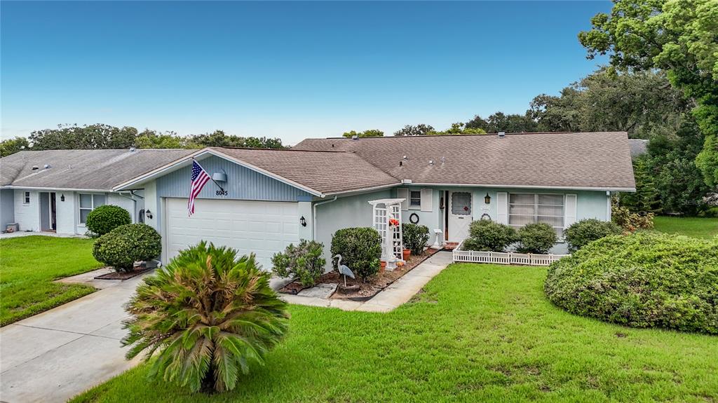 A light blue single-story house with a two-car garage, a lawn, and mature landscaping — 8045 PASADENA DRIVE, PORT RICHEY, FL
