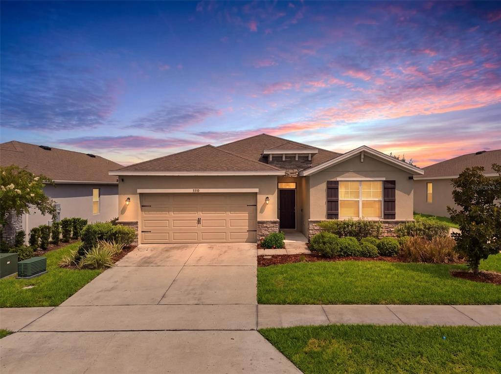 A single-story suburban house with a tan stucco exterior, a two-car garage, and a driveway — 5310 SUNSHINE DRIVE, WILDWOOD, FL