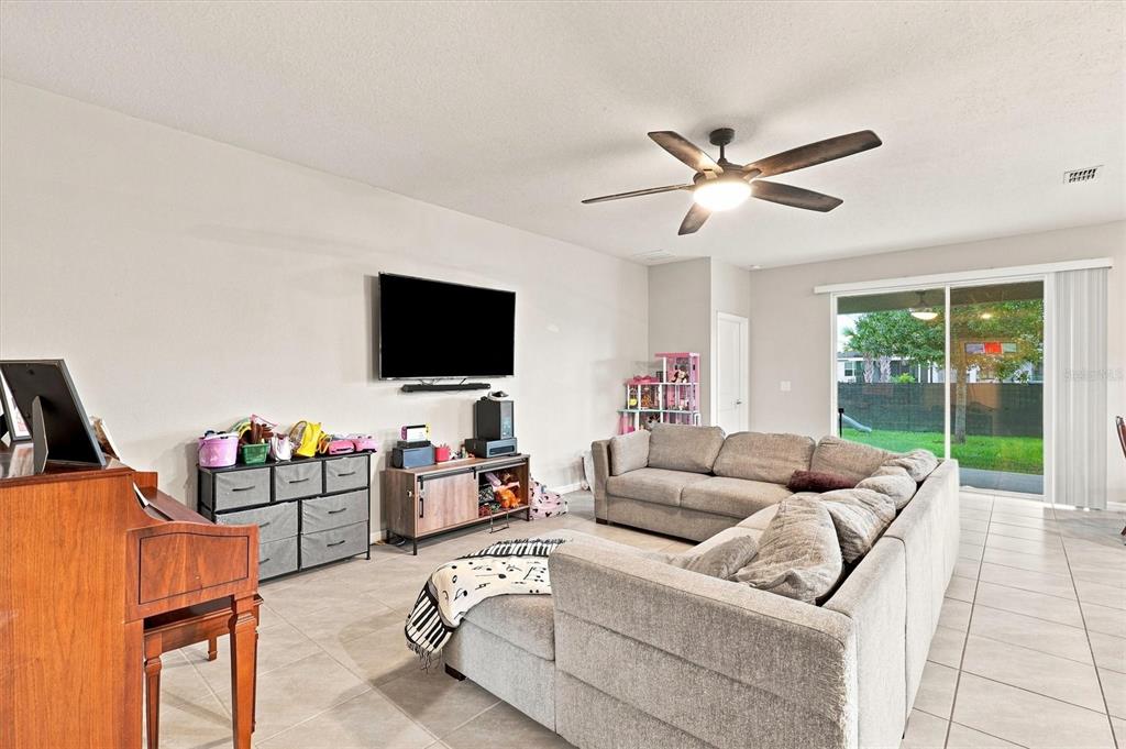 A living room features a sectional sofa, a television, a piano, and sliding glass doors — 5310 SUNSHINE DRIVE, WILDWOOD, FL