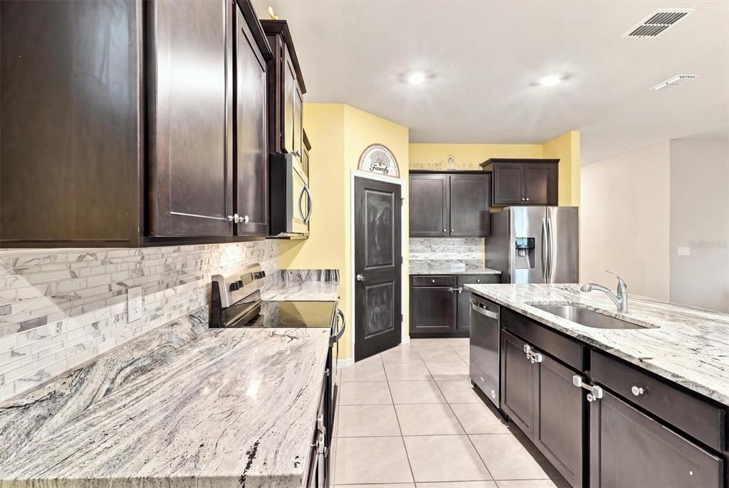 A kitchen features dark wood cabinets, granite countertops, stainless steel appliances, and light tile flooring — 5310 SUNSHINE DRIVE, WILDWOOD, FL