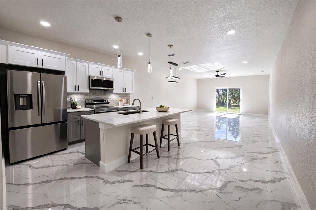 A modern kitchen with white cabinets, stainless steel appliances, and a marble-patterned tile floor — 4818 24TH STREET SW, LEHIGH ACRES, FL
