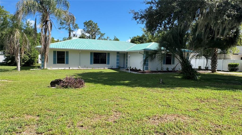 A white single-story house with a green metal roof and blue shutters sits on grass — 5329 EAGLES NEST ROAD, FRUITLAND PARK, FL