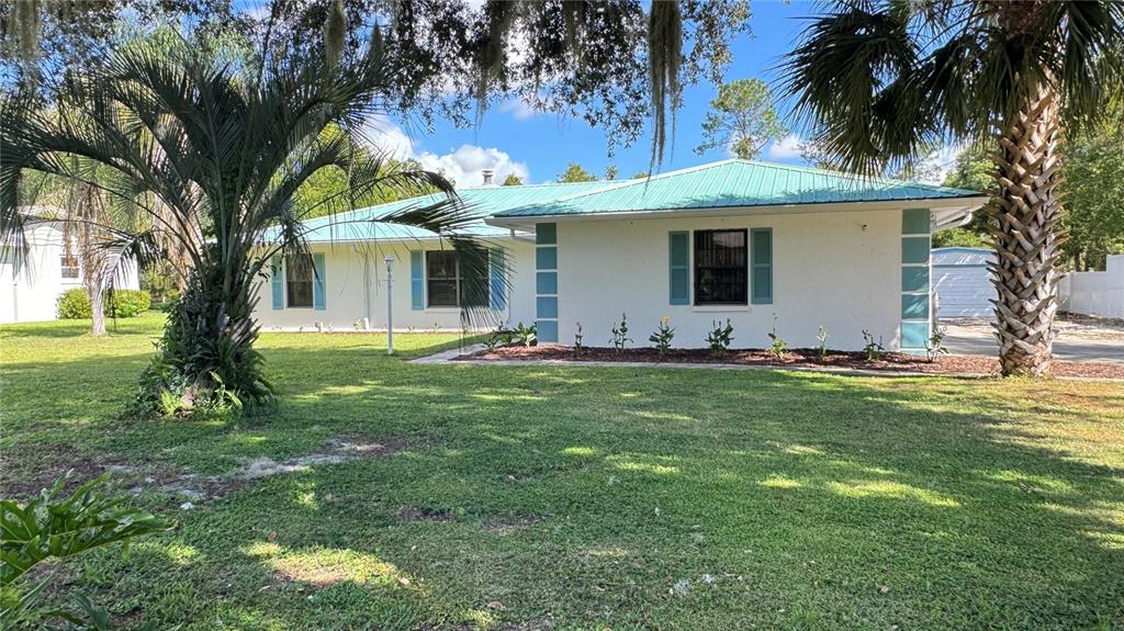 A white single-story house with a green metal roof and blue shutters sits on grass — 5329 EAGLES NEST ROAD, FRUITLAND PARK, FL