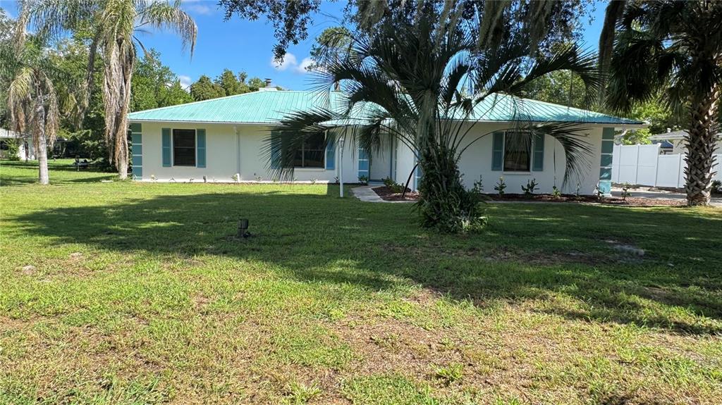 A single-story house with a teal metal roof and white exterior sits on a lawn — 5329 EAGLES NEST ROAD, FRUITLAND PARK, FL