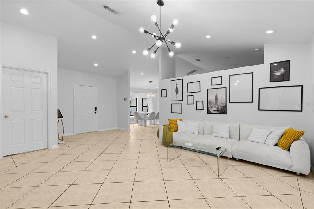 A living room with white walls, tiled floors, a white sofa, and a modern chandelier — 148 VALENTINO COURT, DAVENPORT, FL