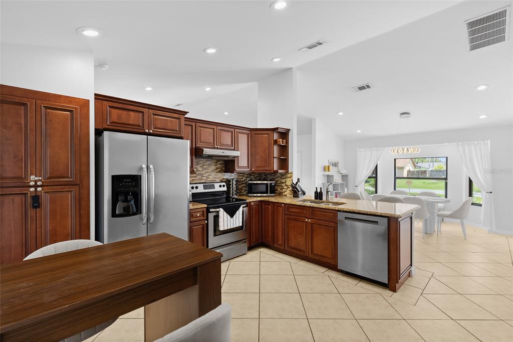 A kitchen with wood cabinets, stainless steel appliances, and a dining area with large windows — 148 VALENTINO COURT, DAVENPORT, FL