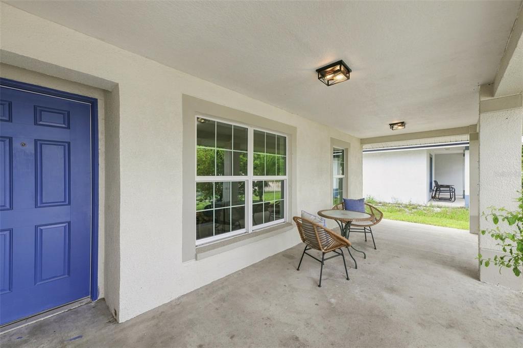 A covered concrete porch features a blue front door, a window, and patio furniture — 1116 SHARED PASSION STREET, RUSKIN, FL