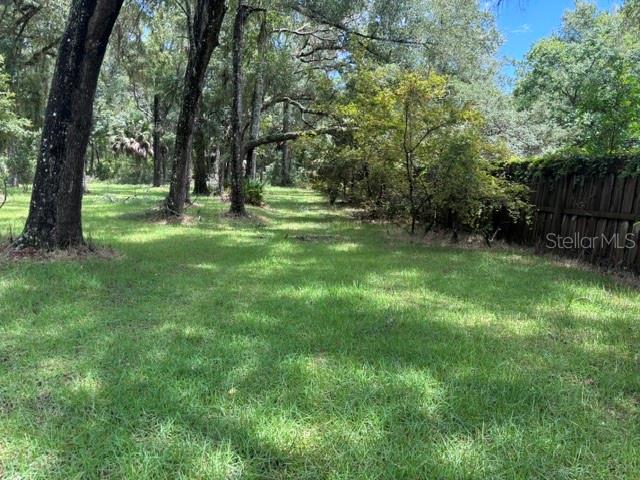 A grassy backyard features mature trees and a wooden fence along the right side — 7455 NW 95TH STREET, CHIEFLAND, FL