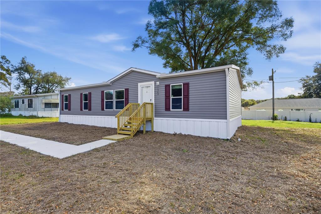 A single-story manufactured home with grey siding, white skirting, and a wooden front staircase — 1560 NE 162ND STREET, CITRA, FL