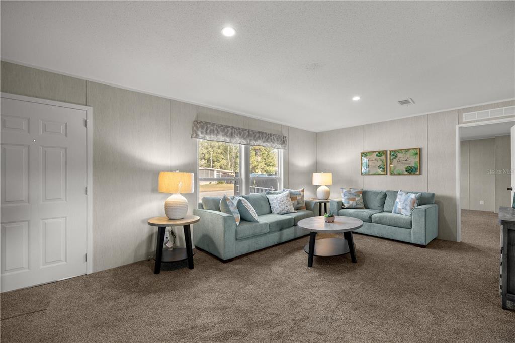 A living room features light wood-paneled walls, brown carpeting, two teal sofas, and a coffee table — 1560 NE 162ND STREET, CITRA, FL