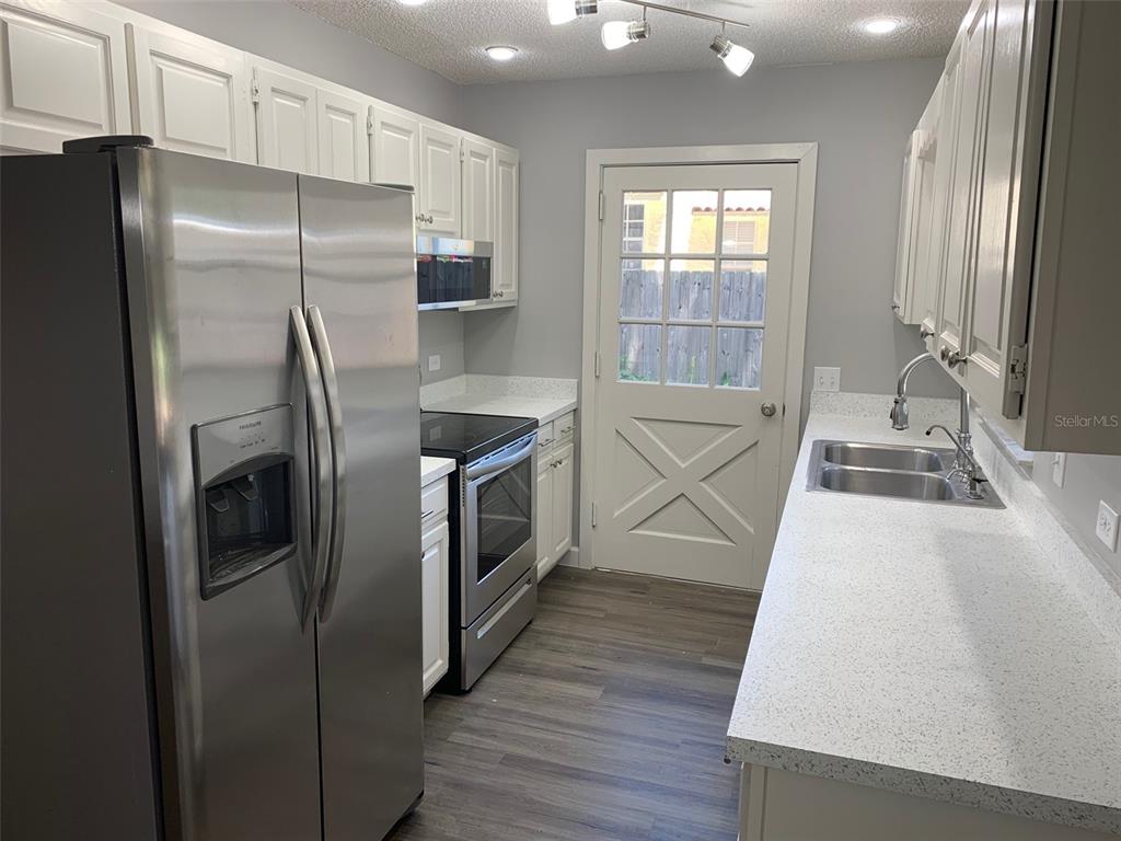 A kitchen features white cabinets, stainless steel appliances, speckled countertops, and a glass-paneled exterior door — 527 HILL STREET UNIT A, EUSTIS, FL